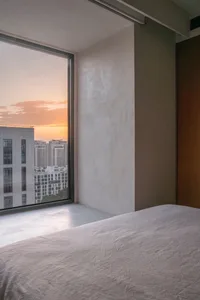 Minimalist bedroom with concrete walls and a view of the sunset through a large window.