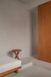 A minimalist bedroom featuring a wooden bed and concrete walls, creating a serene and modern atmosphere.