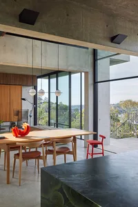 Modern dining room with concrete walls, wooden dining table, and red accents.