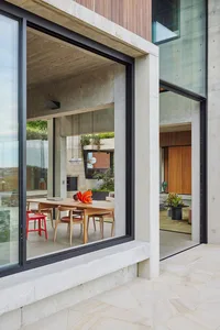 A modern interior living room with concrete walls and floor, featuring wooden furniture and large windows.