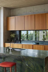 A modern kitchen with a green marble countertop and wooden stools.