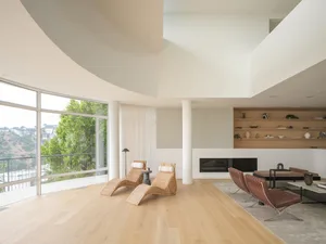 A modern living room featuring wooden floors, large windows, and comfortable seating areas.