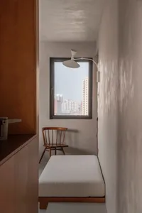 A minimalist bedroom with concrete walls, wooden furniture, and a fabric cushion on the floor.