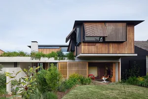 A modern house featuring a combination of concrete and wood exteriors, with a greenery rooftop and a partially open wooden ga