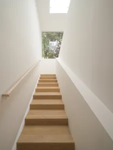 Modern minimalist stairs with wooden steps and light-colored walls leading to a bright window.