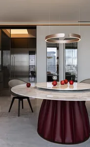 A modern kitchen featuring a round marble table with apples and a contemporary pendant light fixture.
