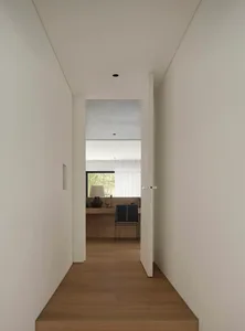 A minimalist hallway with wooden flooring and white walls, featuring a door leading to another room.