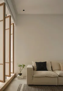 A minimalist living room featuring a grey fabric sofa, a wooden floor lamp with white paper screens, and a small potted plant