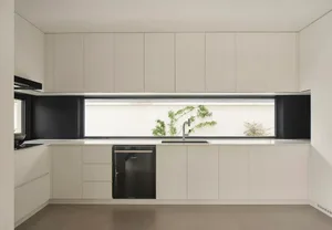 A modern, minimalist residential kitchen with white cabinets, black accents, and a large window showcasing outdoor greenery.