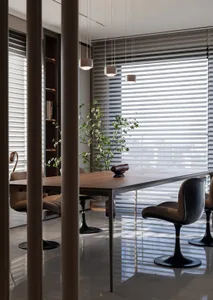 A modern dining room featuring a wooden table with black chairs, minimalist decor, and large windows with blinds.