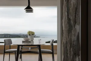 A modern dining table with a marble top and fabric upholstered chairs, set against a backdrop of a cityscape and ocean view.