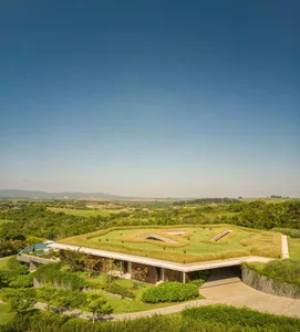 A modern residential home with a green roof surrounded by lush greenery and a clear blue sky.