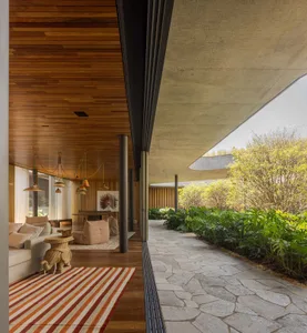 Modern industrial living room with concrete flooring, wooden ceiling, and large windows overlooking greenery.