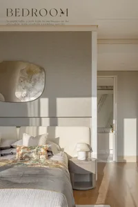 A modern, neutral-toned bedroom features a stone floor, marble accents, and a large bed with patterned pillows.
