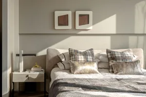A modern bedroom featuring neutral textiles on the bed and a side table with a lamp and books.