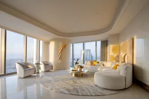 A modern living room with white marble flooring, a circular rug, a beige sectional sofa, cream-colored armchairs, a round cof