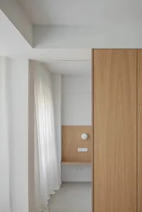 A minimalist apartment interior with wooden cabinets and white window treatments.