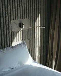 A minimalist bedroom with a concrete textured wall and a white pillow on a bed.