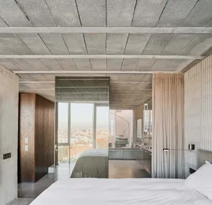 Modern bedroom with concrete walls and ceiling, featuring a bed with white sheets and a glass partition.