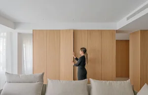 A woman in a modern living room with wooden walls and a light gray sofa.