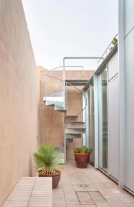 Modern metallic spiral staircase outside a building with a glass wall.