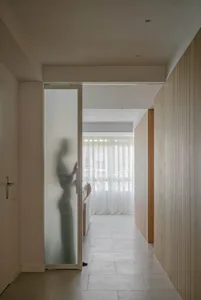 A modern minimalist interior with white marble flooring, frosted glass sliding door, and light-colored wooden walls.
