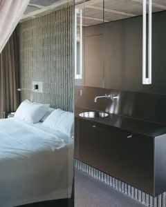 Modern minimalist bedroom featuring a metal vanity sink, white linens, and a textured wall behind the bed.