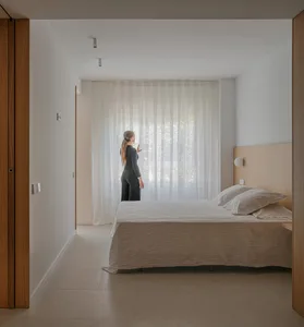 A bedroom featuring minimalist design with textured wood, white textiles, and translucent curtains.