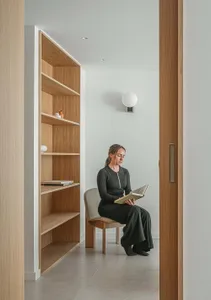 A woman sitting on a wooden chair in a minimalist library, holding a book.