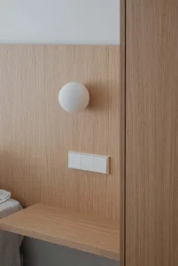 A modern oak bedside table with a white spherical lamp and minimalist wall switches.
