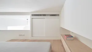 A minimalist bedroom with white walls and wooden accents, featuring a bed with white bedding.