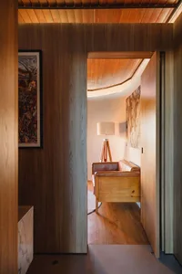 A modern living room with wooden furnishings and a lamp, viewed from an adjacent hallway.