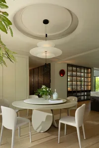 A modern, minimalist dining room with a round table, chairs, vases, and a decorative red wall light, featuring sleek, clean l