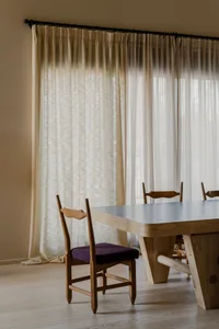 A minimalist dining room featuring wooden furniture and sheer curtains.