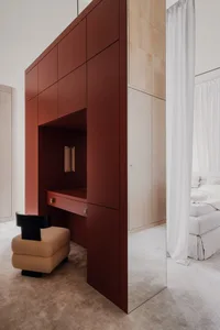 A modern bedroom featuring a dressing table with red cabinets and a beige upholstered stool.