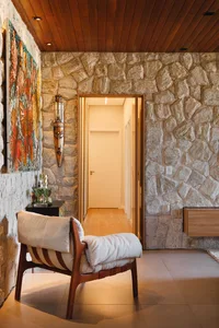 A modern residential entryway featuring a stone and brick wall, a wooden chair, and a colorful painting.