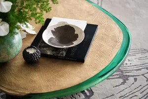 A modern coffee table with a green glass edge, featuring decorative items including a vase with flowers, a black candle, a bo