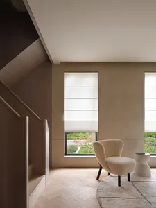 A modern living room featuring a tan stone floor, beige carpet, textured white walls, white curtains, and a white chair with 