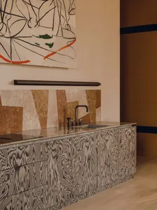 A modern interior space featuring a wooden counter with a sink and faucet, surrounded by abstract artwork and a mix of neutra