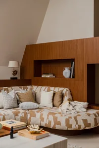 A modern living room with a patterned sofa adorned with cushions and a wooden backrest. Books and a vase decorate the niche.