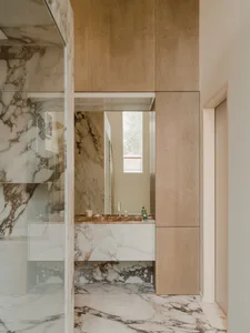 A sleek, contemporary bathroom with marble tiles, a glass shower enclosure, and wooden cabinetry.
