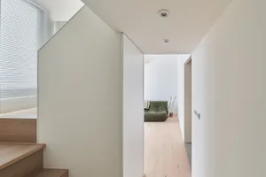 Modern minimalist hallway with wooden stairs, glass wall, and concrete floor.