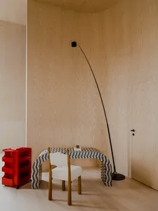 A modern workstation with a unique curved desk, a white upholstered chair, and a red rolling cart with transparent drawers in