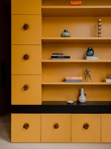 A modern storage shelf with yellow painted cabinets and drawers, featuring decorative objects and books.