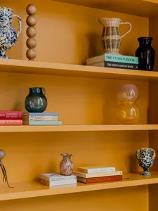 Three shelves adorned with colorful ceramics, glassware, and books.