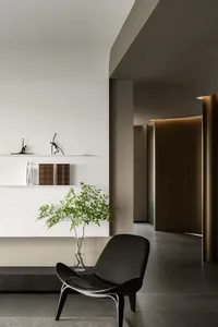 Minimalist living room with concrete floor and wall, featuring a black leather armchair, a plant in a vase, and a shelf with 