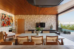 Modern residential dining room featuring wooden furniture, stone walls, and a television on a stone wall.