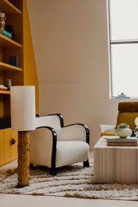 A modern residential living room featuring a textured fabric armchair, a coffee table with books and a vase, and a yellow boo