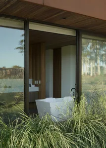 Minimalist bathroom with concrete walls and white freestanding bathtub surrounded by green plants.