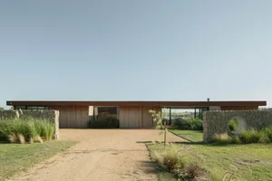 Modern residential home featuring a wood and stone exterior with large windows and a gravel driveway.